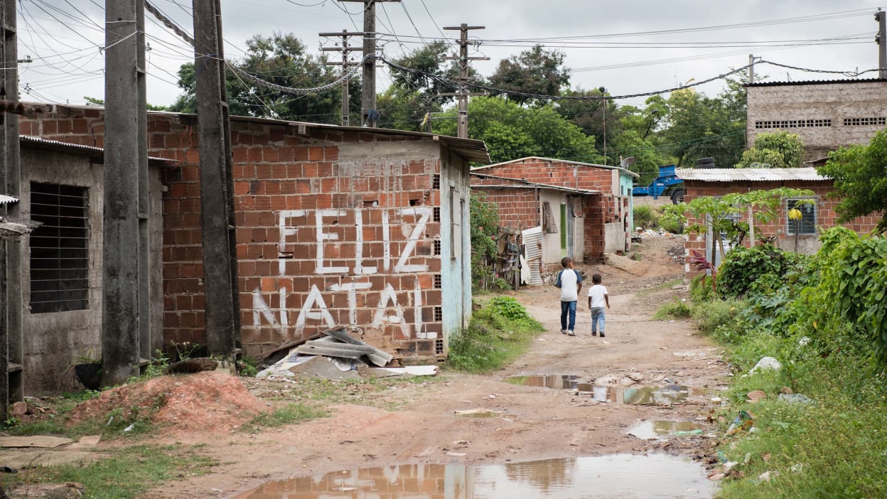 Dos niños caminan por un camino de tierra lleno de baches en una favela en Brasil construida entre torres de energía. Las palabras “Feliz Navidad” (“Feliz Natal”) adorna una de las viviendas.