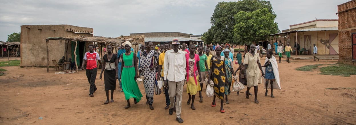 A group of people walk through a village in South Sudan