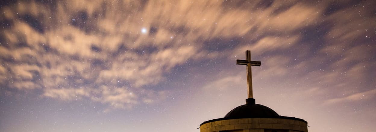 Church dome and cross against sky at dusk