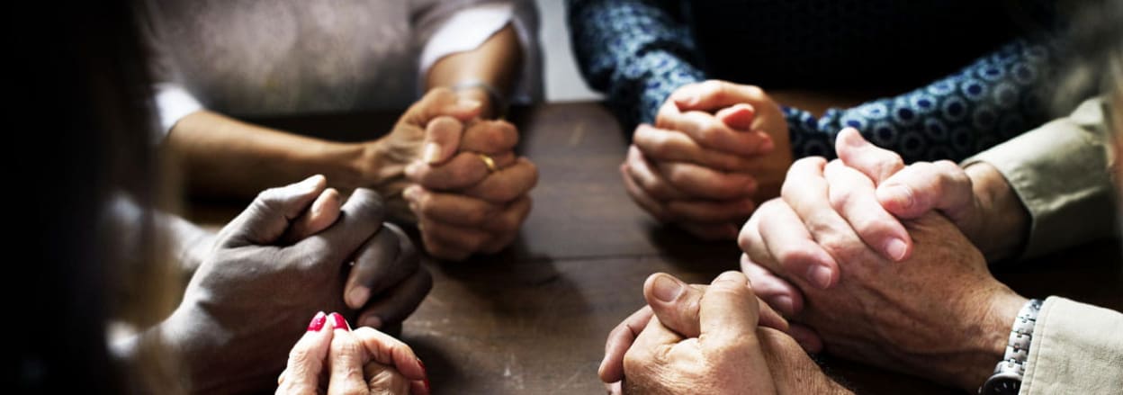 Praying hands around a table
