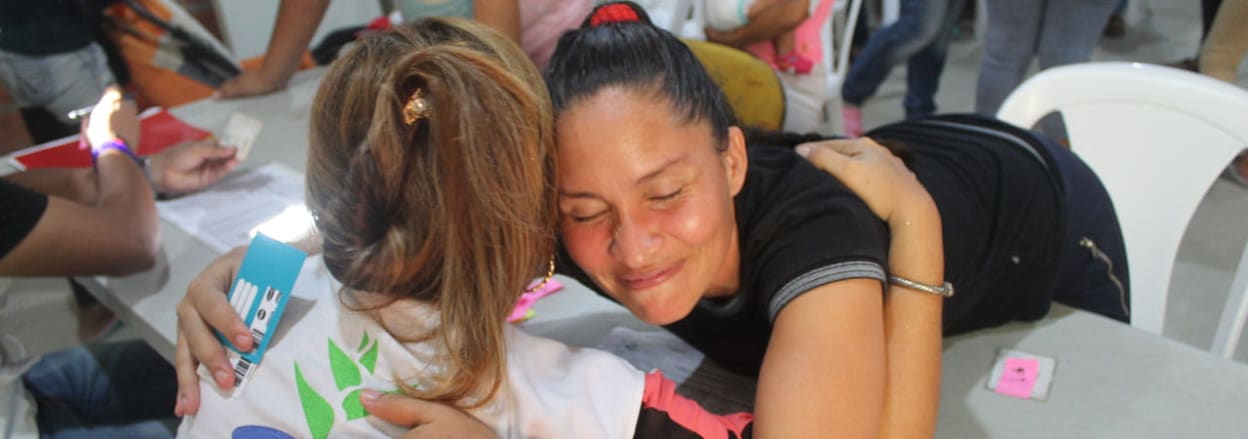 Venezuelan migrant hugs church volunteer across desk.