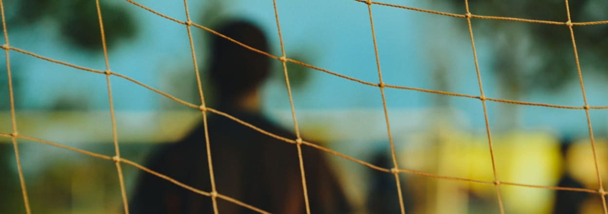 picture of goalkeeper from behind net (Photo by Dan Gold on Unsplash)