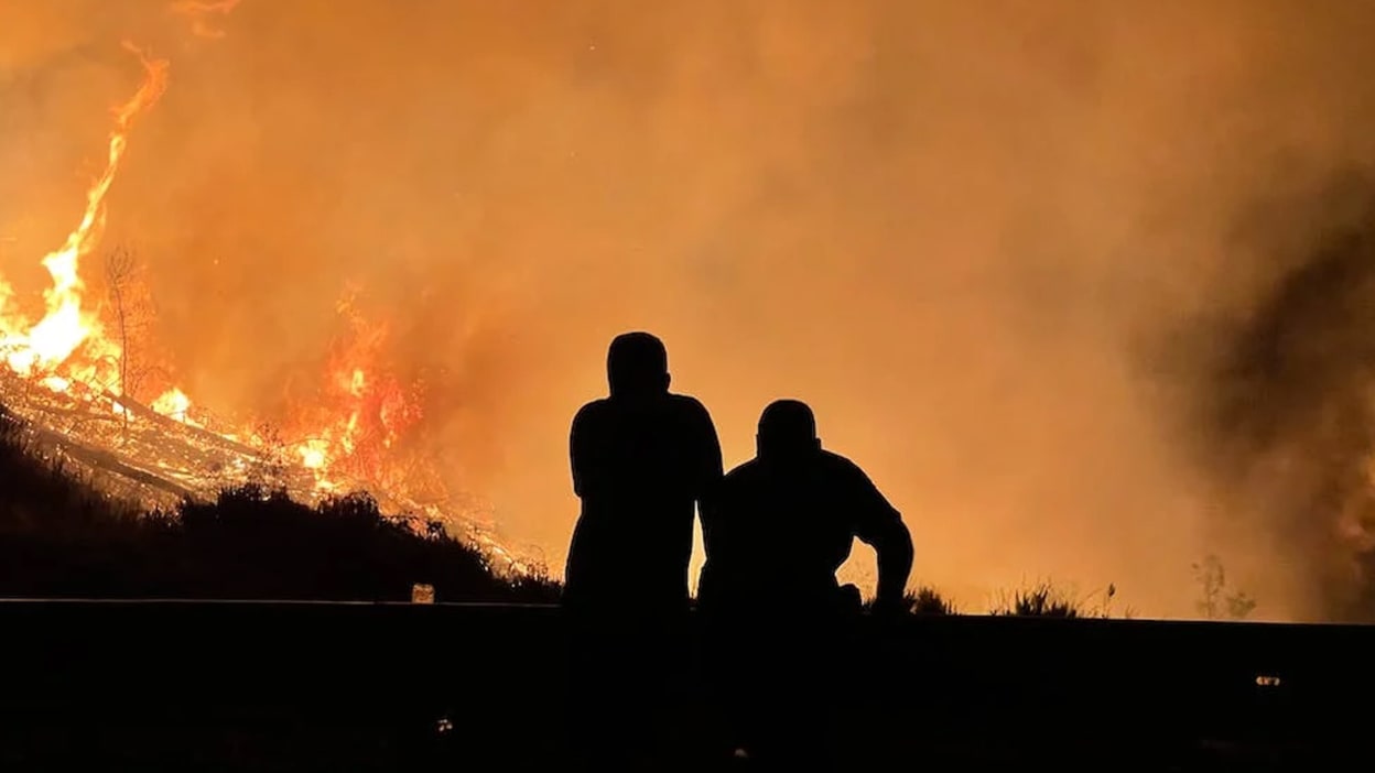 Silhouette of two people sitting with a burning building in the background