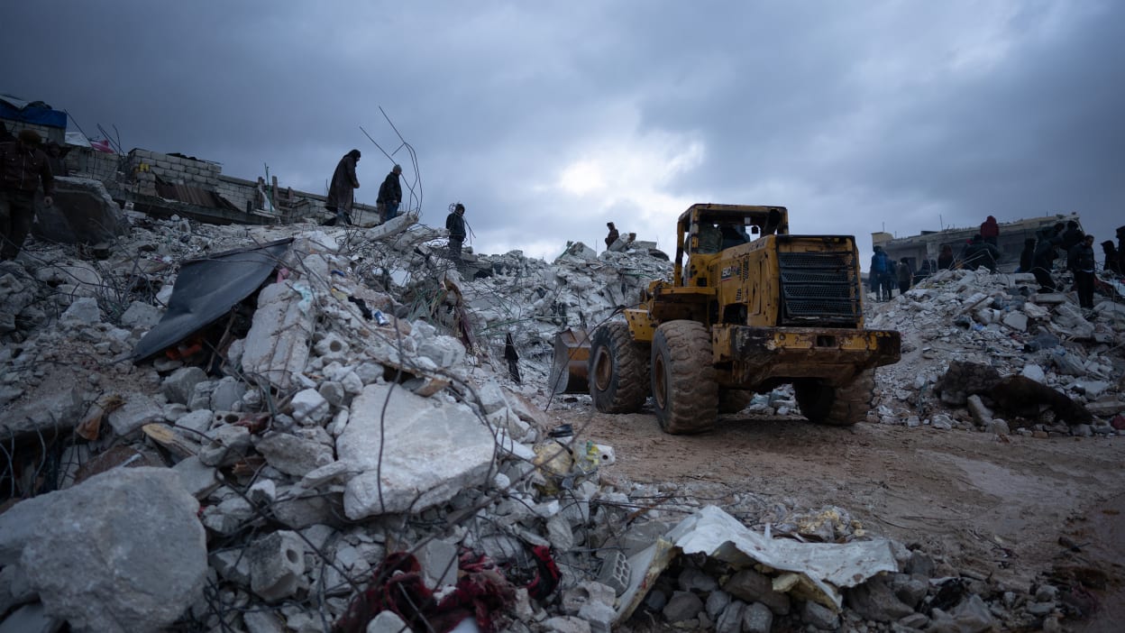 A digger parked in front of a large pile of rubble