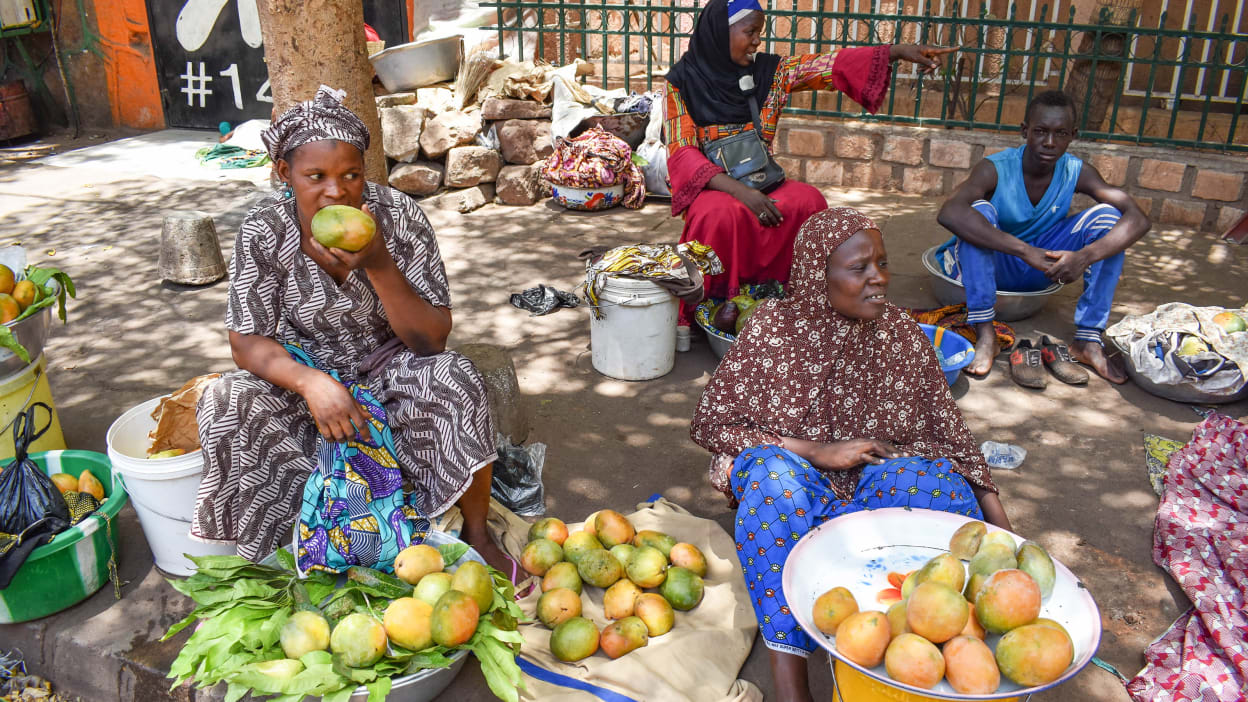 Three women sell fruit on a shaded pavement in Mali