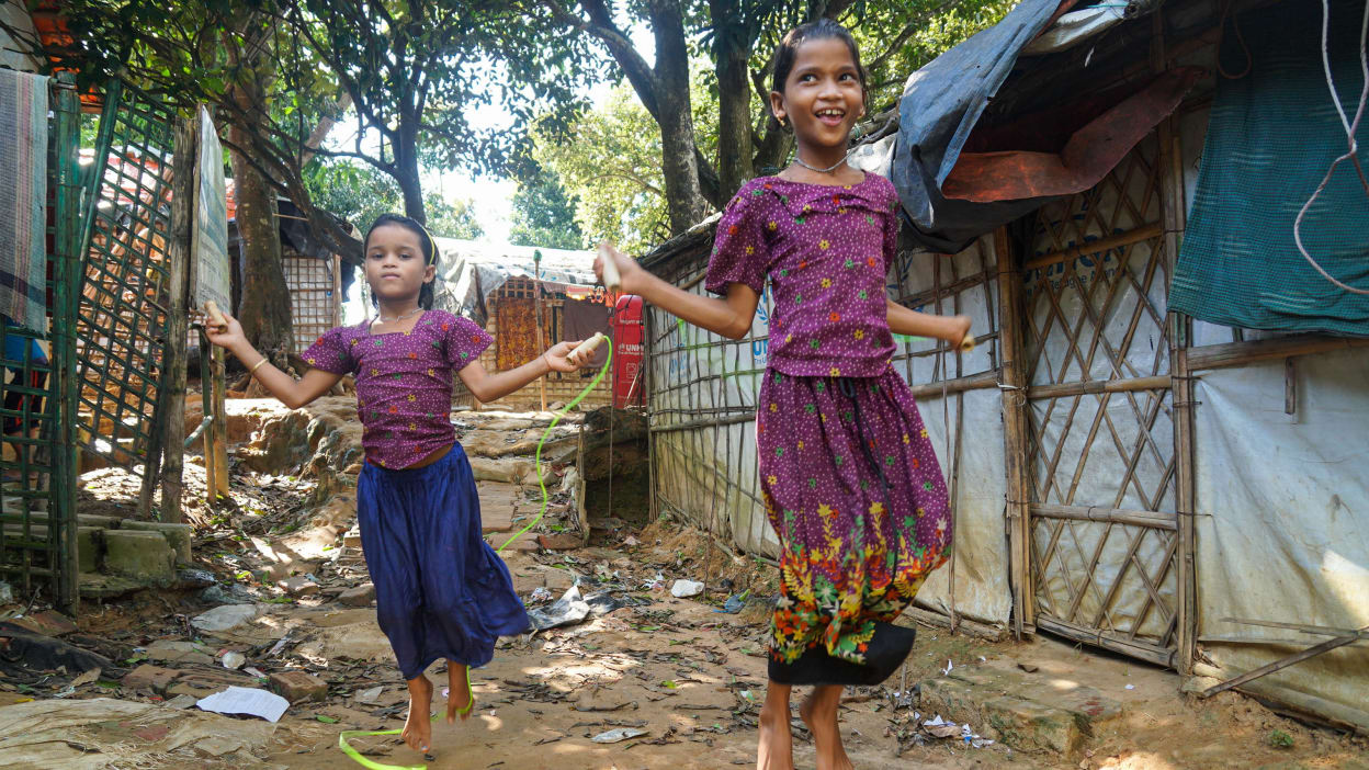 Two young girls in bright clothes play in the dusty path outside tents that form part of the world's largest refugee camp, Cox's Bazar, Bangladesh.