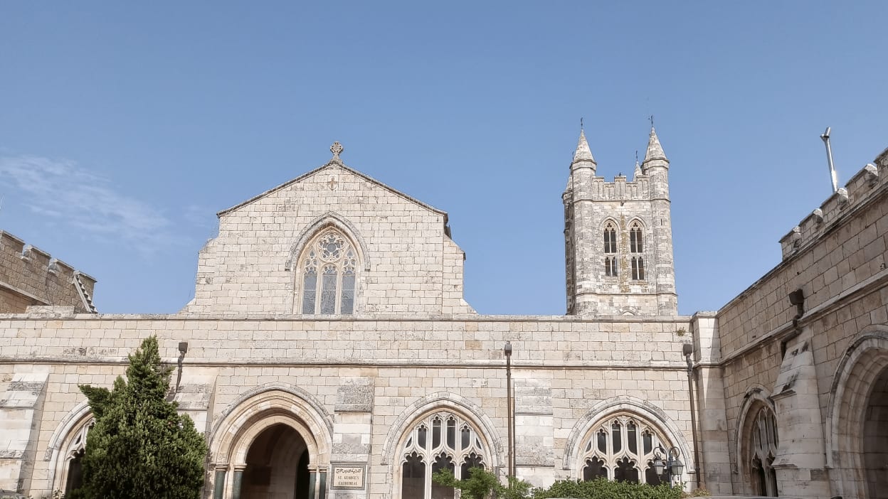 The ornate pale stonework of St George's Cathedral stands against a pale blue sky in Jerusalem. 