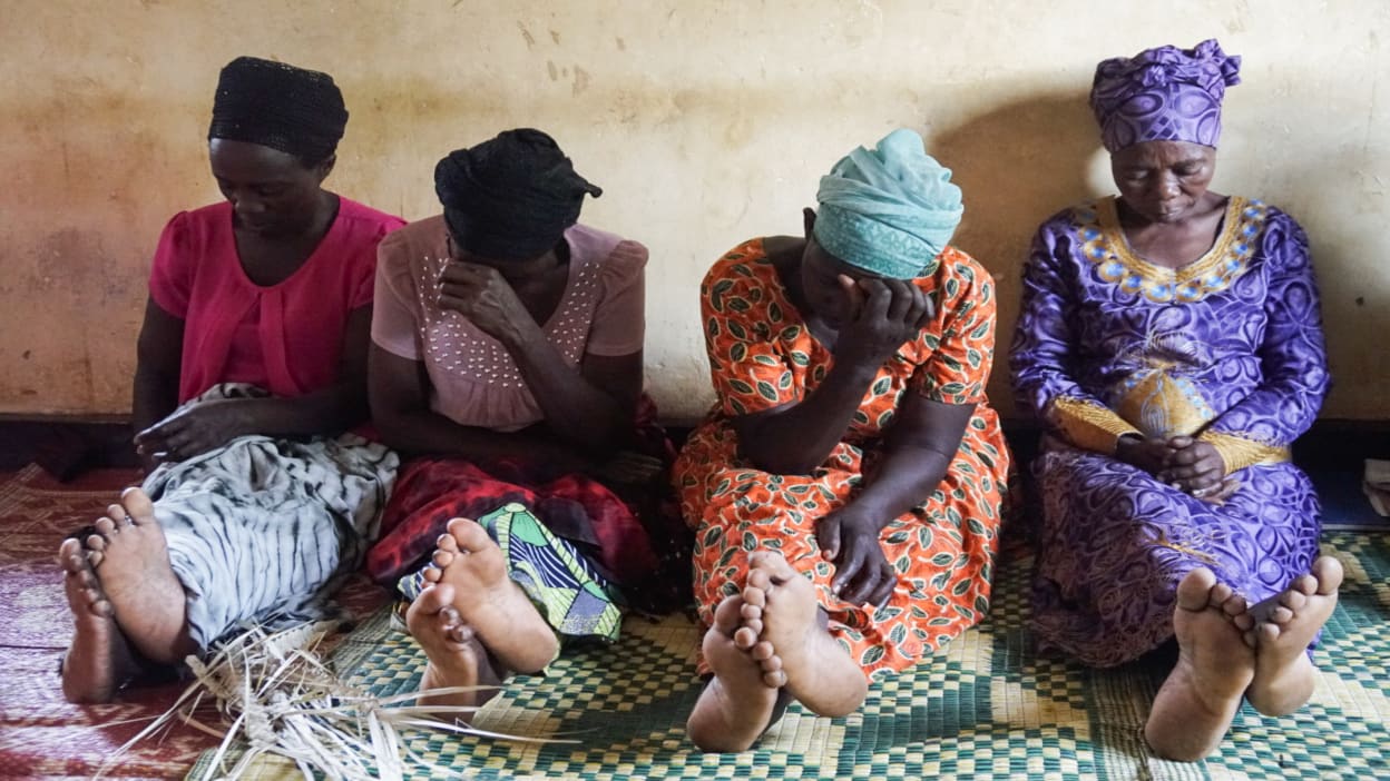 Four women in colourful clothing sit together on a mat praying. They are part of a self-help group set up by Tearfund's local partner in Rwanda as part of Church and Community Transformation programming. 