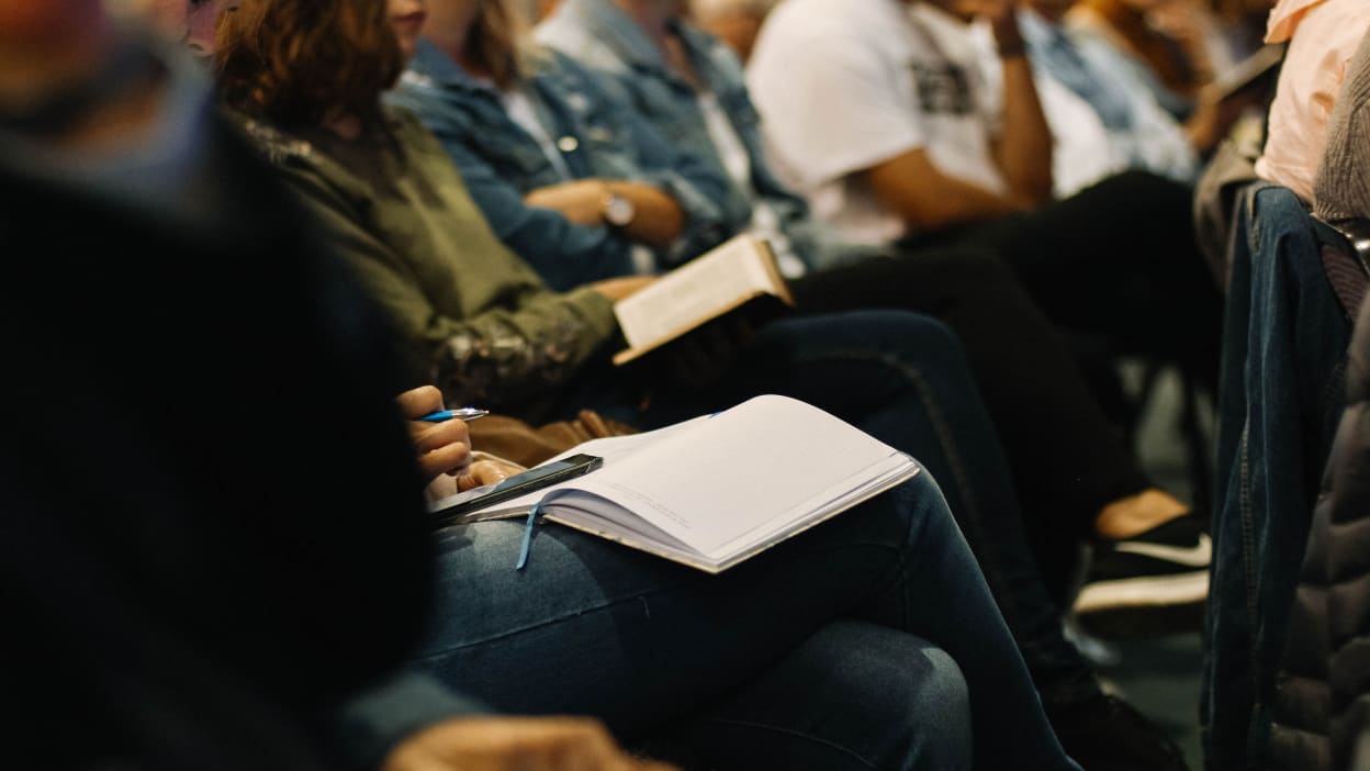 A row of people listen to a talk with notebooks and Bibles in their hands.