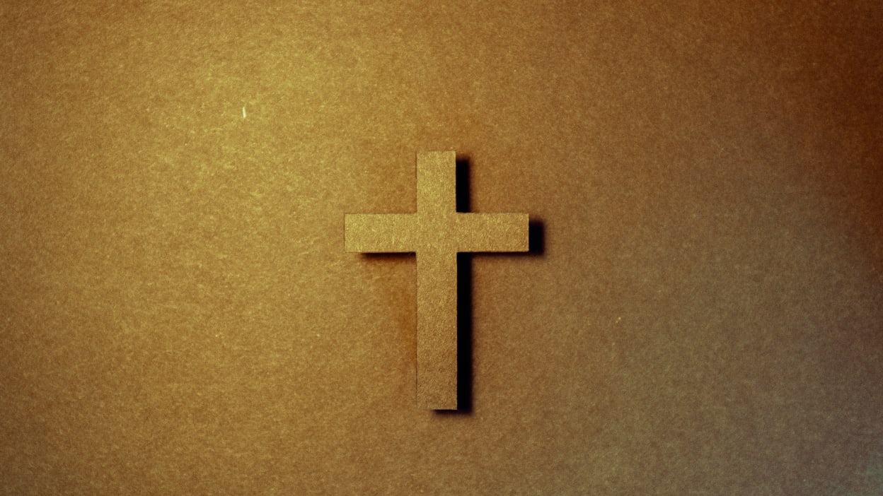 A brown wooden cross against a wooden background. 