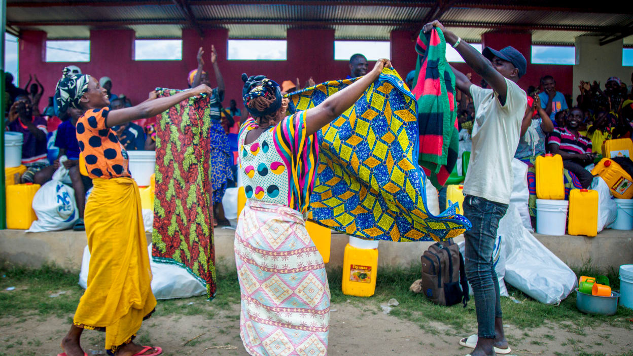 Two women and a man happily hold up colourful blankets they received as part of support after flooding destroyed people's homes and belongings in Burundi.