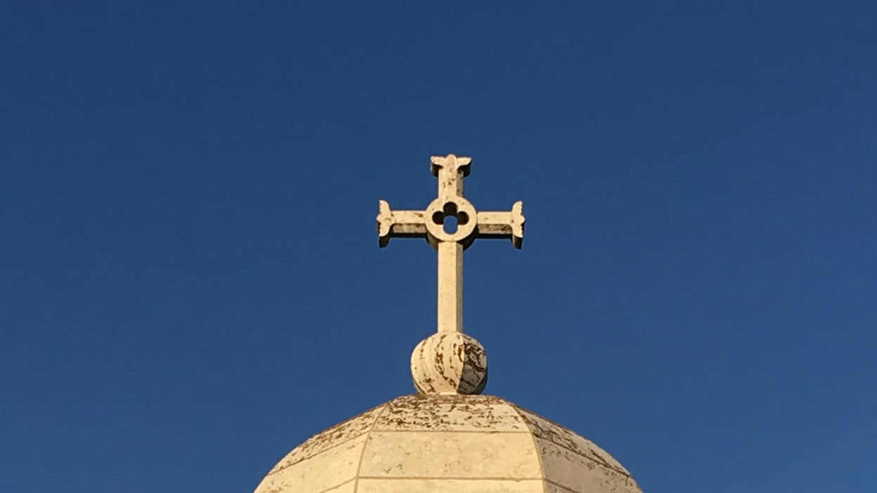 A white cross on top of a domed church against a blue sky