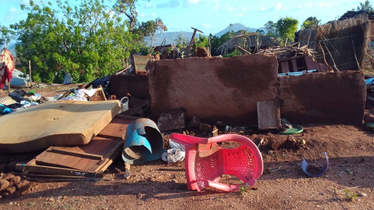 A red plastic chair, a mattress and other household items lie strewn across the ground in front of houses destroyed by Cyclone Chido in Mozambique.