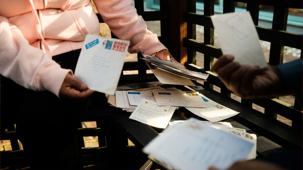 Two people sort through letters on a bench between them.