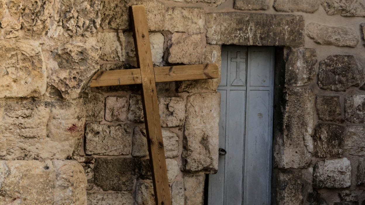 A wooden cross leans against a rocky wall next to a door with a cross embossed in the top.