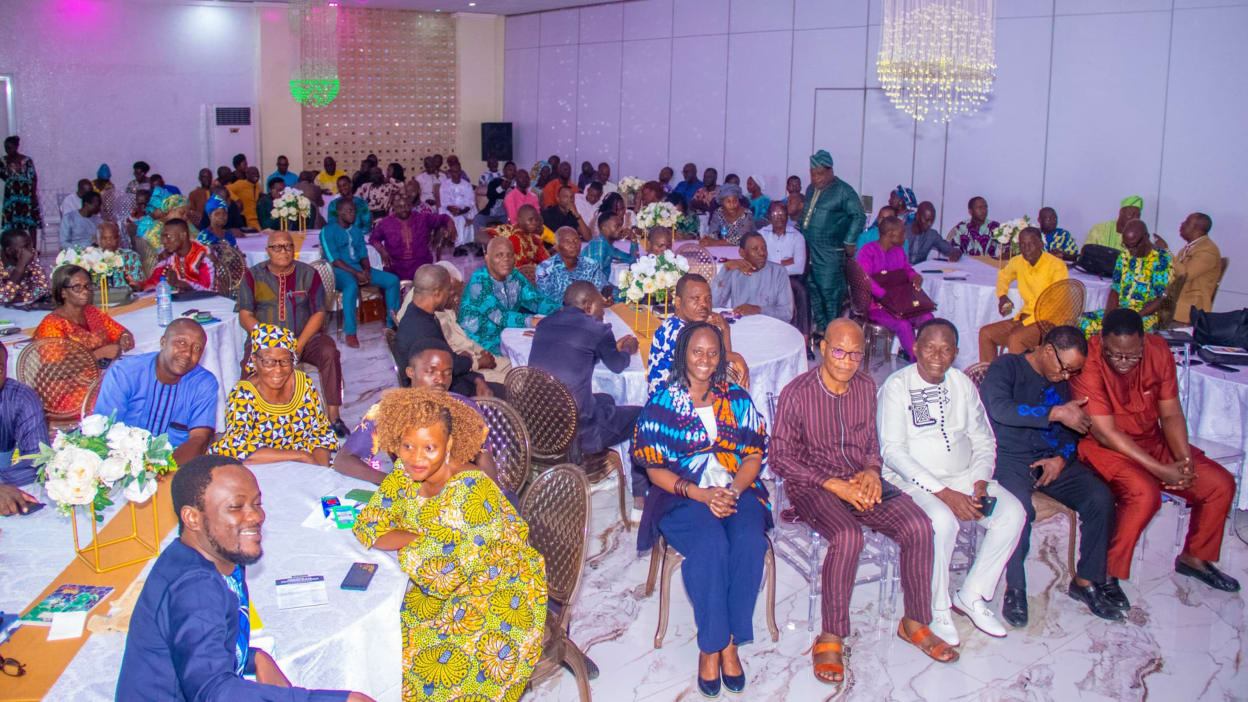 A room full of people sat on chairs at large round tables. 