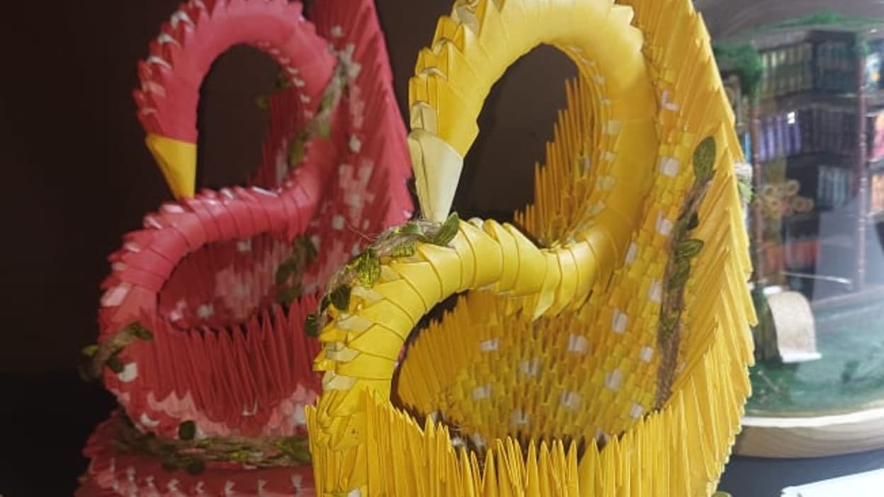 Two intricately crafted swans, made of folded pieces of paper, sit next to each other on a work surface.