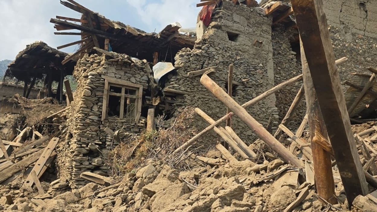 wood and stone rubble in front of the remains of a house that has been destroyed by the earthquake in Afghanistan 