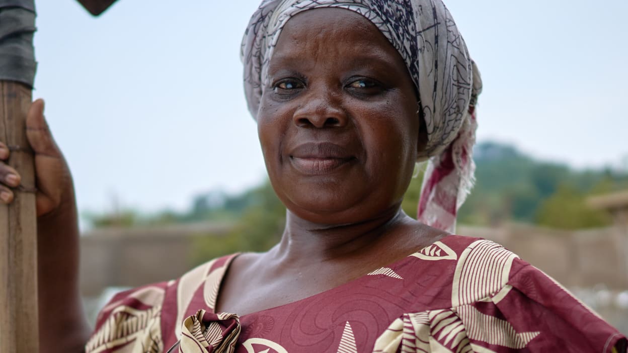 Portrait of a smiling African woman wearing headscarf and patterned dress, holding a pole.
