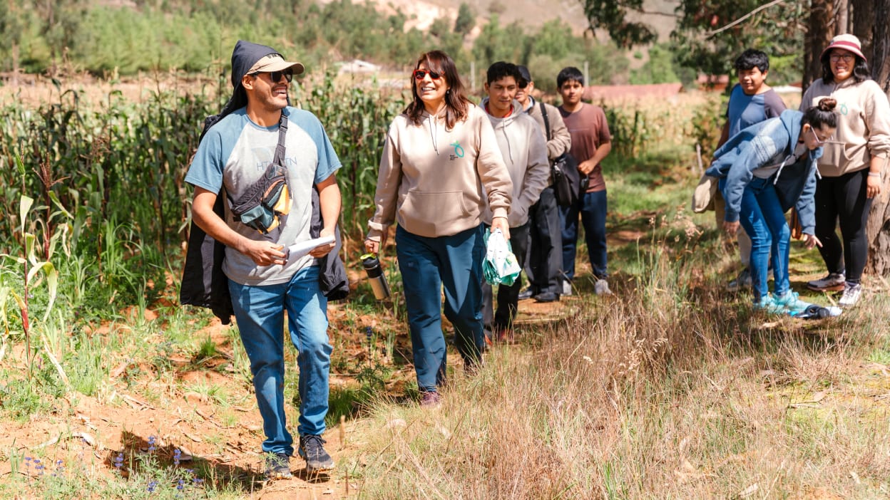 Group hiking through a field; adults and children on a dirt path surrounded by vegetation.