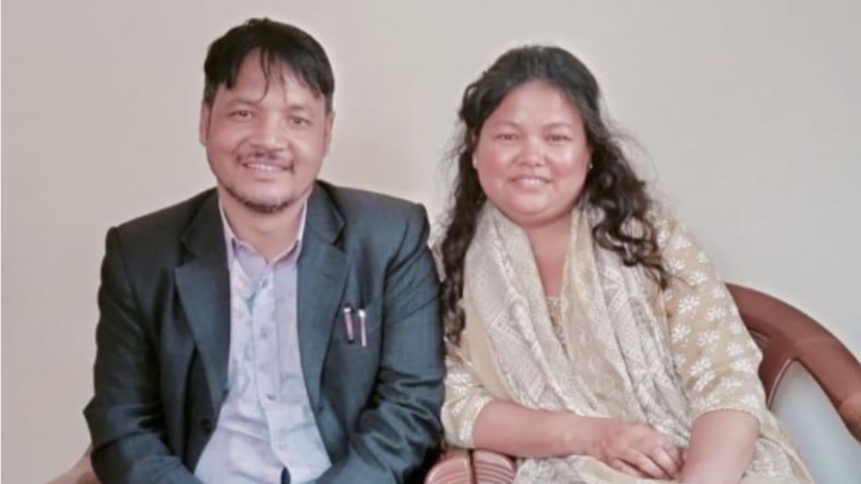 A man and a woman are sitting closely side-by-side, both smiling gently at the camera.