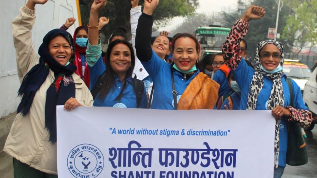 Group of women with fists raised holding a Shanti Foundation banner protesting stigma/discrimination.