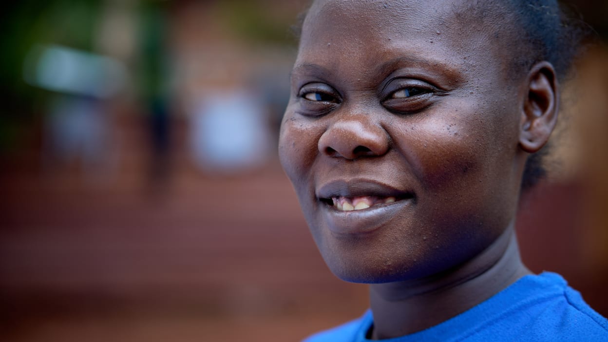 Portrait of a smiling Black woman with dark skin and a blue shirt, against a blurred background.