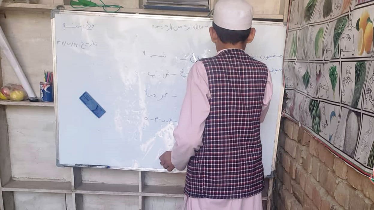 A boy Ali* stands and writes on a whiteboard in a classroom.