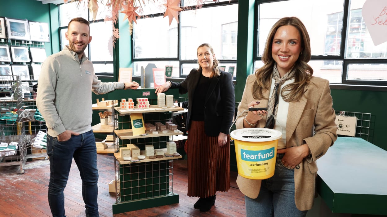 Elanna Magowan (Influencer and Founder of Pearl Beauty) holding a Tearfund collection bucket. Feature in the background are Chris Thompson (Tearfund NI Director) and Bronagh Luke (Corporate Marketing Controller, Henderson Group)