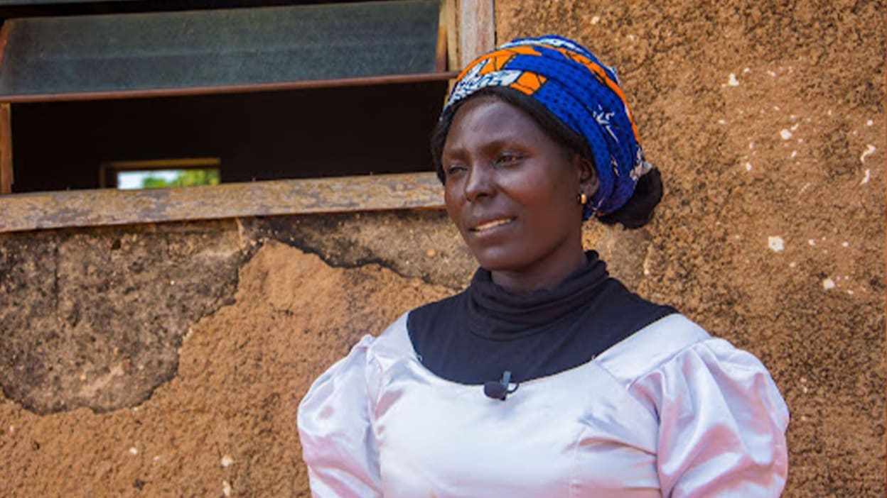 A portrait of Nankyer, a school teacher in Nigeria. She wears a blue and orange headscarf, and a dress. She is being interviewed about her story.