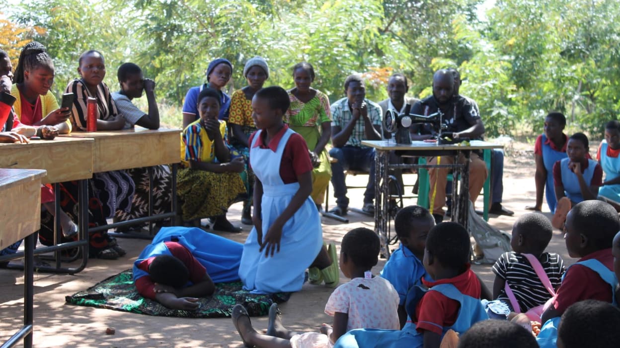 Group of students and adults gathered outdoors; sewing machine present.