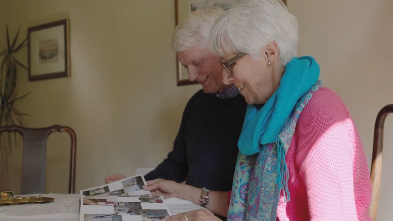 A smiling elderly couple sitting at a table looking at photographs