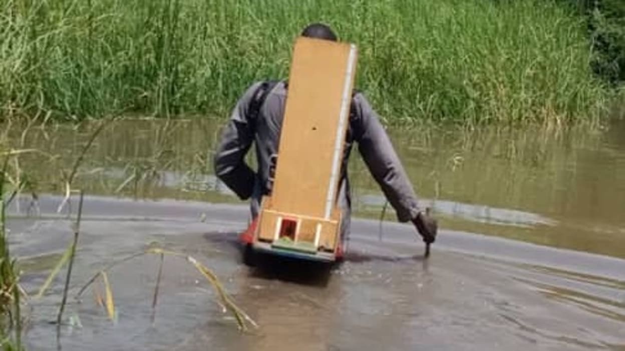 One of Tearfund’s nutrition officers walks through the deep floodwaters, carrying a height board on his back, one of the tools used to assess children for malnutrition.