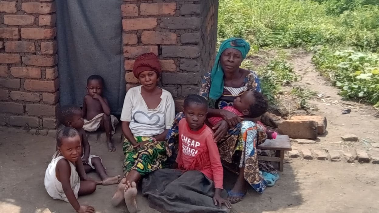 Christine and her family members, including four young children, sit outside their home.
