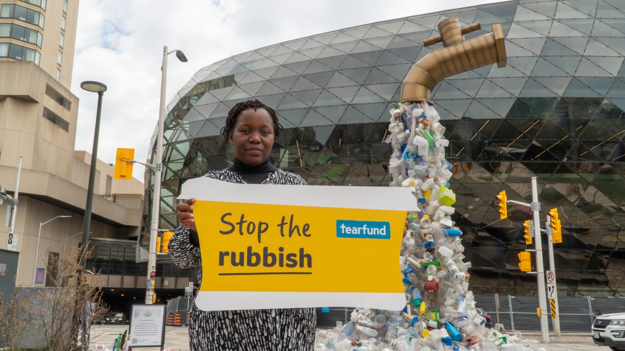 Dr Tiwonge Mzumara Gawa stands with a poster saying 'Tearfund: stop the rubbish'