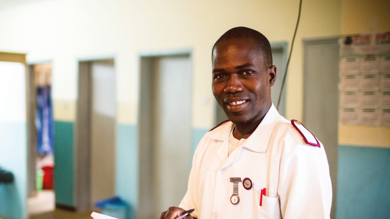 Um agente de saúde malawiano vestindo seu uniforme branco e vermelho e sorrindo para a câmera enquanto toma notas