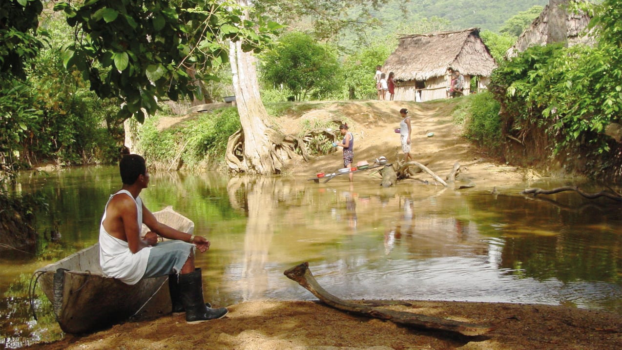 Un homme assis dans un vieux bateau de pêche en métal regarde vers la rive d’un fleuve dans une campagne du Honduras.