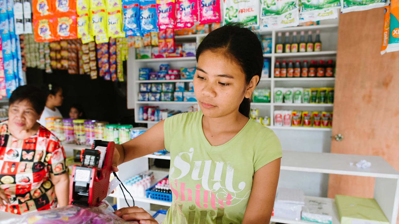 Une jeune fille en t-shirt vert se sert d’une machine pour étiqueter un article dans un magasin.