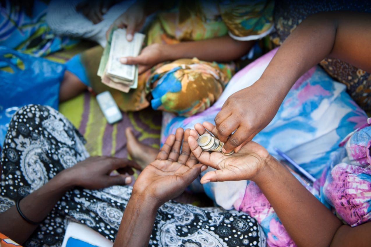 Two ladies in Ethiopia hold out their hands and share coins with each other against a background of colourful clothing.