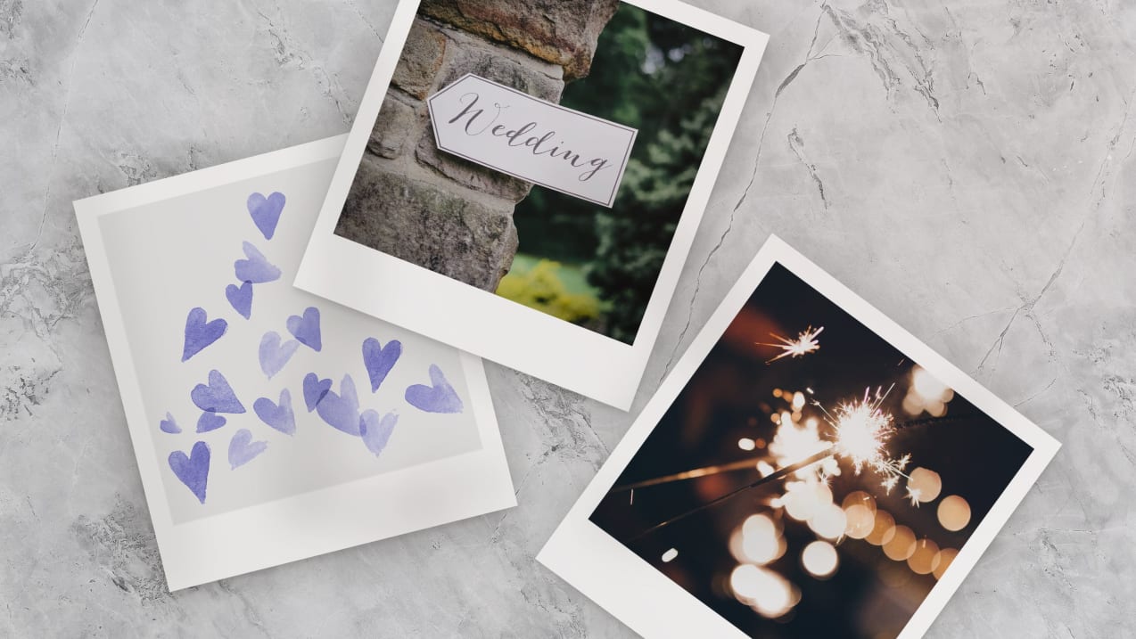 Three polaroid photos are spread across a white rough surface. One photo is of painted purple hearts scattered around. Another photo is of a sign with the word "wedding" on a wall. The third photo is of several lit sparklers in the dark. 