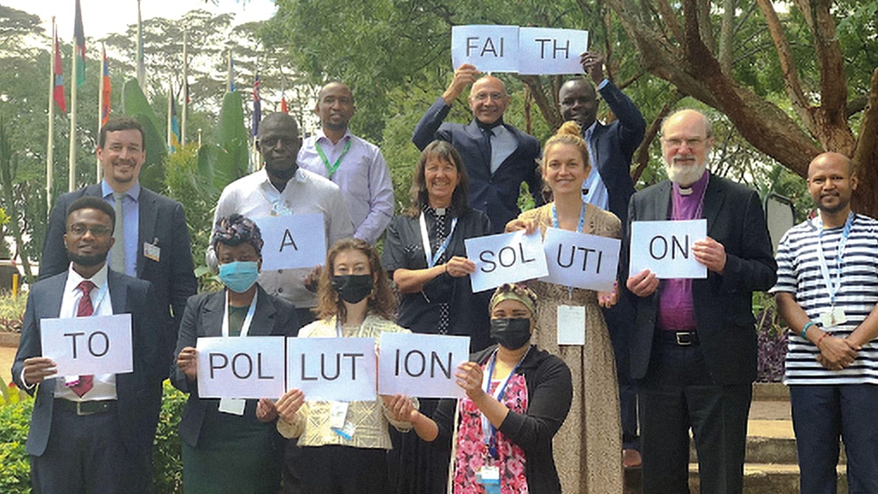 A group of people holding sheets of paper which spell out 'Faith a solution to pollution'