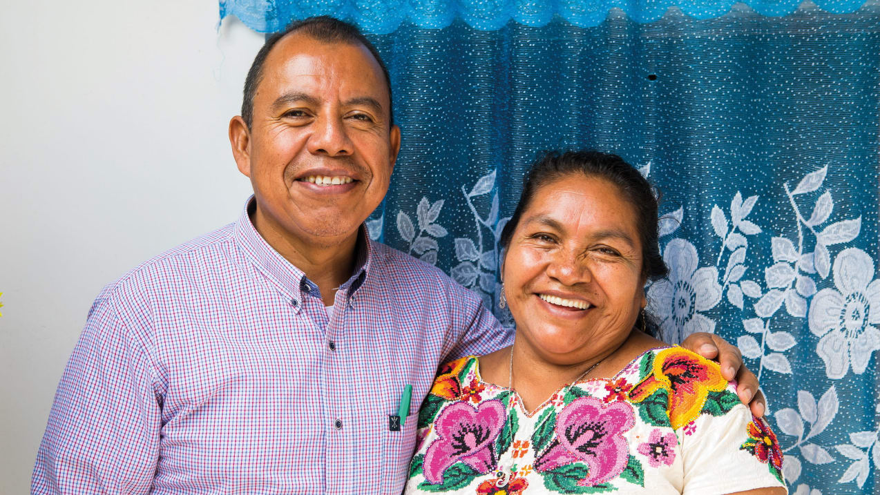 A man and woman smile at the camera, with their arms around each other's backs.