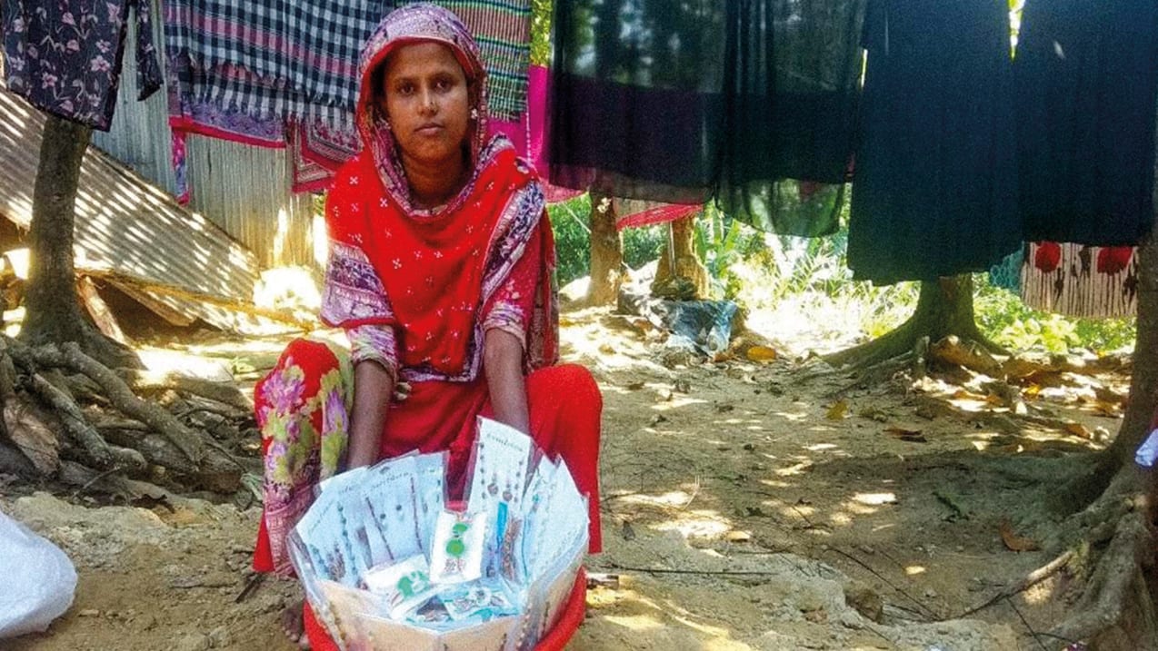 A woman sitting outside with a variety of packaged garlands and hung laundry in the background