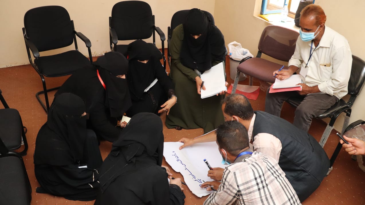A group of people sitting in a circle, writing on a large piece of paper