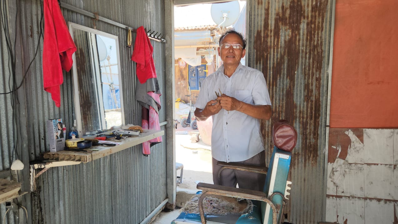 A man standing in the door of a barber shop with corrugated metal walls