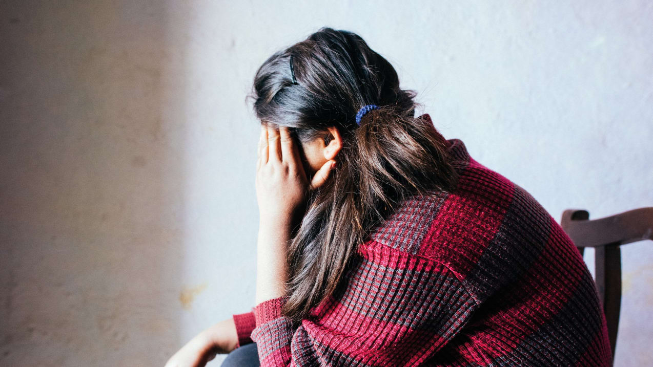 A woman sitting in a chair covering her face with her hand
