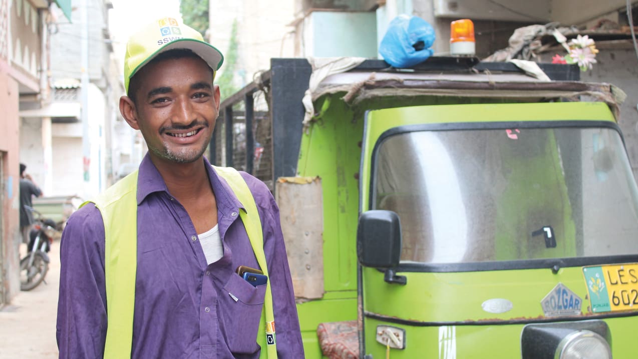 A man dressed in a high-vis vest and cap is stood in front of a green truck.