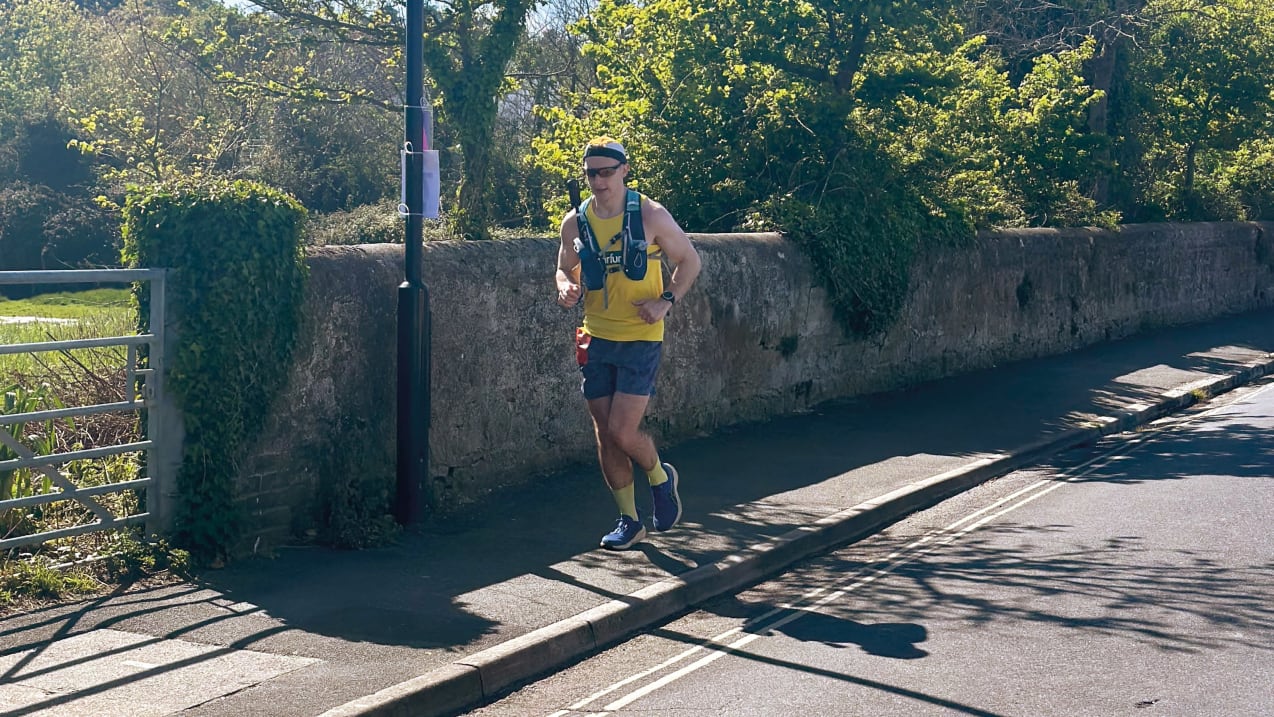 A man dressed in a yellow Tearfund vest top and running gear is running along a pathway beside a road.