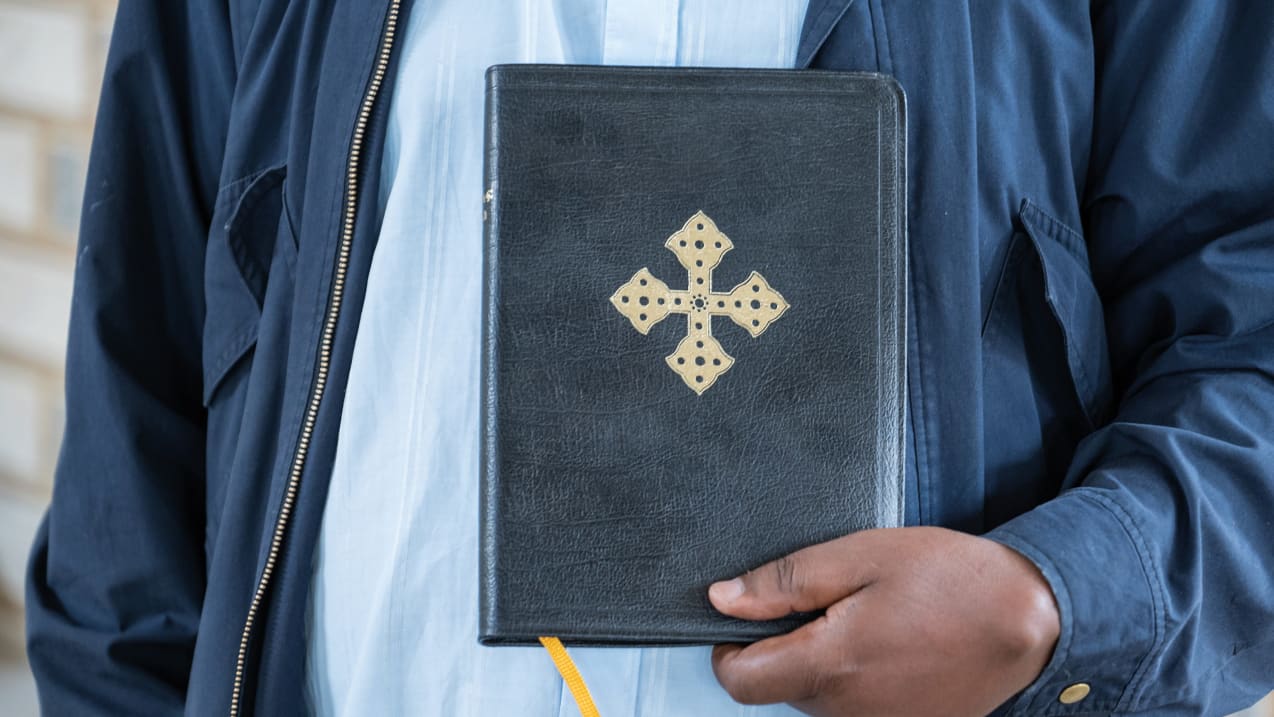 Someone holds up a bible in front of their chest with one hand. 