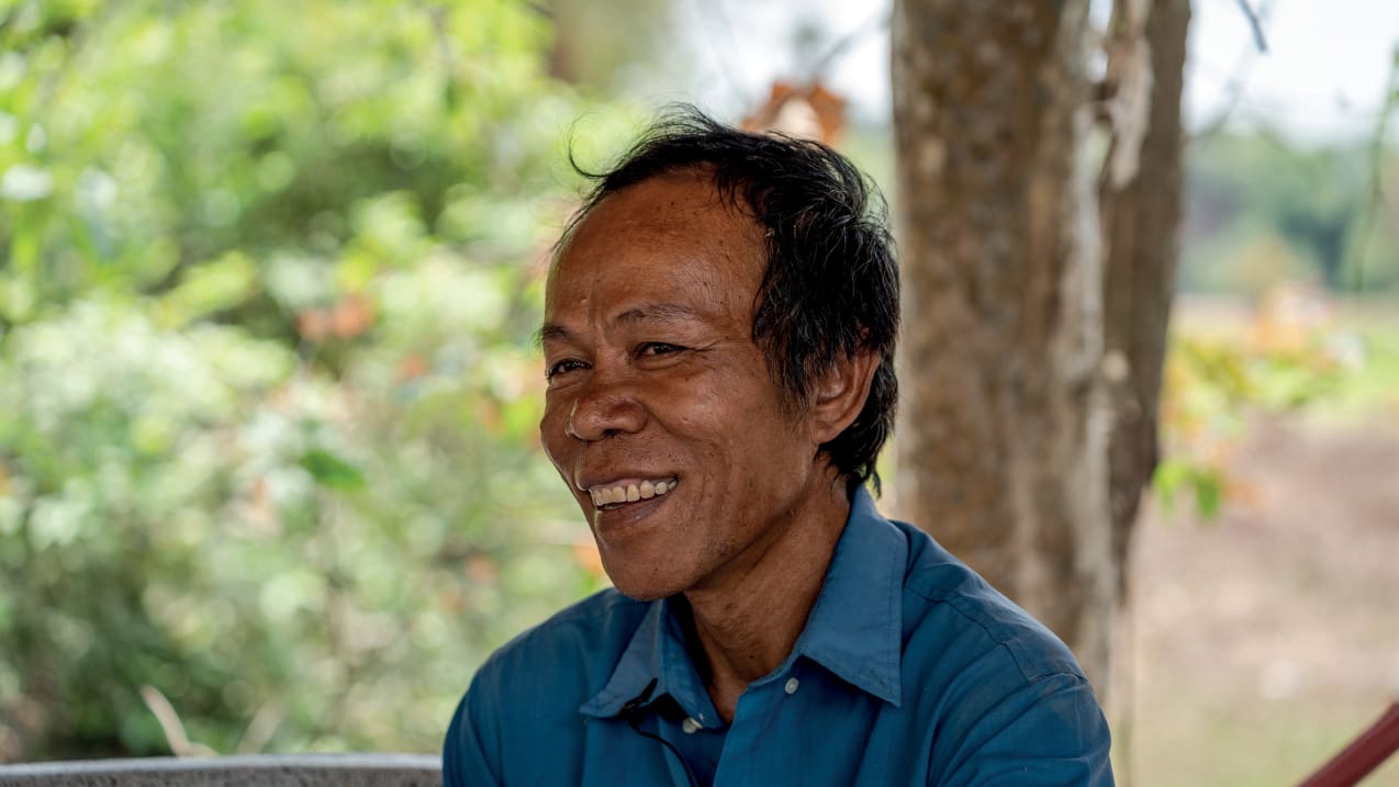 A man dressed in a shirt looks to the side and smiles.